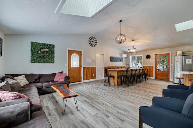 982 Long Ridge Rd, Hawley, PA 18428 - living room with a notable chandelier, vaulted ceiling with skylight, light wood finished floors, wood walls, and wainscoting
