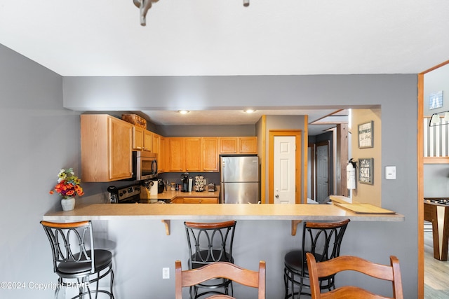 kitchen featuring stainless steel appliances, a peninsula, light countertops, light brown cabinetry, and a kitchen bar