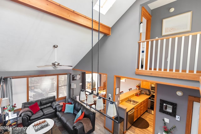 living room featuring a skylight, ceiling fan, wood finished floors, high vaulted ceiling, and beam ceiling