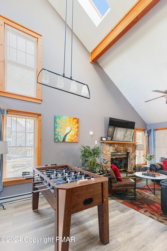 rec room with a ceiling fan, beam ceiling, a stone fireplace, and wood finished floors