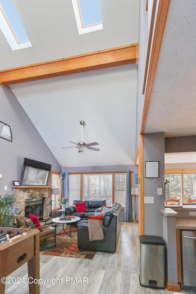 living area featuring a ceiling fan, a stone fireplace, wood finished floors, high vaulted ceiling, and beamed ceiling