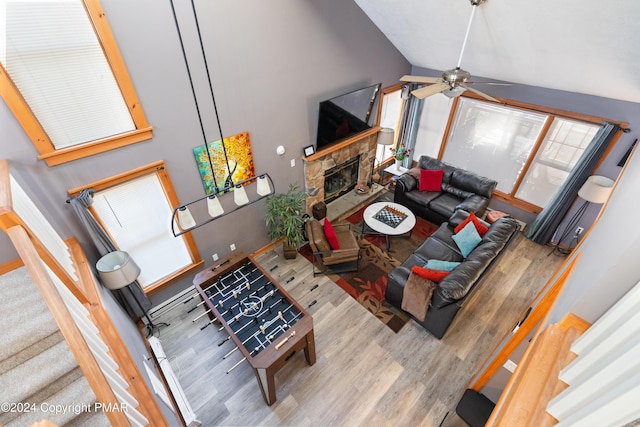 living area featuring high vaulted ceiling, a stone fireplace, and wood finished floors