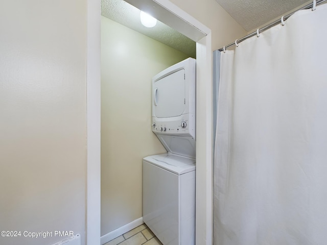 laundry room featuring a textured ceiling, laundry area, light tile patterned flooring, and stacked washer and clothes dryer