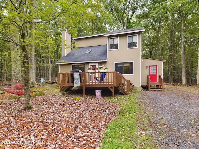 rear view of property with a deck, entry steps, a chimney, and a forest view