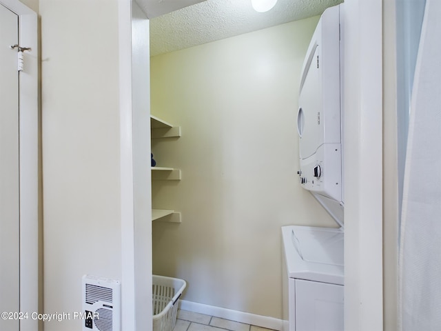 laundry room featuring laundry area, baseboards, a textured ceiling, stacked washing maching and dryer, and light tile patterned flooring