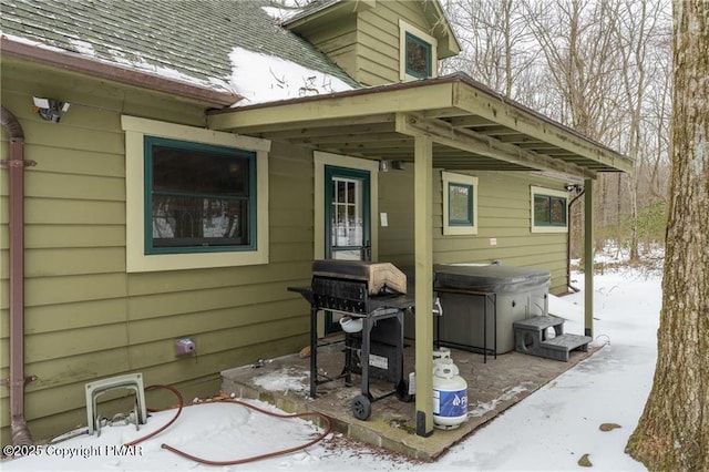 snow covered patio with grilling area and a hot tub