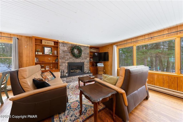 living room with built in shelves, light hardwood / wood-style floors, a baseboard radiator, wooden walls, and a fireplace