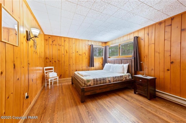 bedroom featuring wood walls, wood-type flooring, and a baseboard heating unit