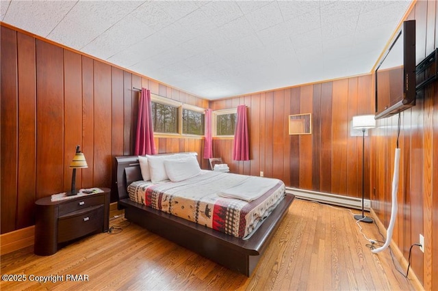 bedroom with a baseboard heating unit, wood walls, and light hardwood / wood-style flooring