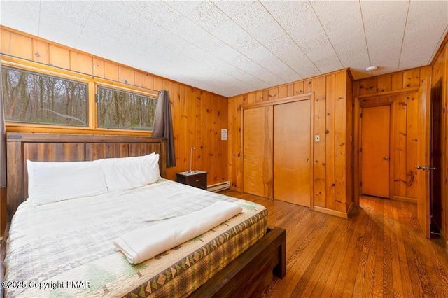 bedroom featuring a baseboard heating unit, a closet, wood walls, and dark hardwood / wood-style floors