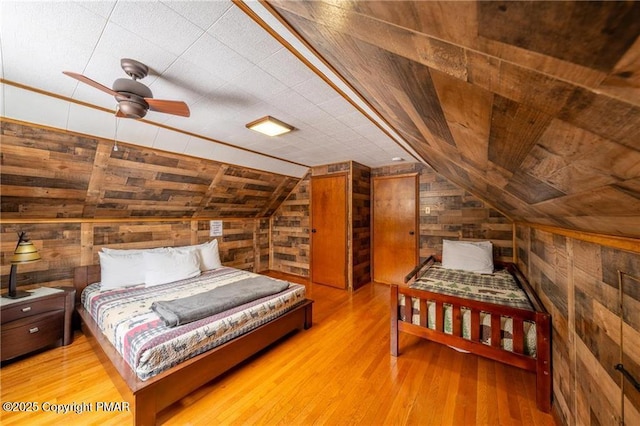 bedroom featuring light hardwood / wood-style floors, lofted ceiling, and wooden walls