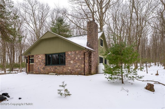 view of snow covered exterior featuring stone siding, a chimney, and a garage