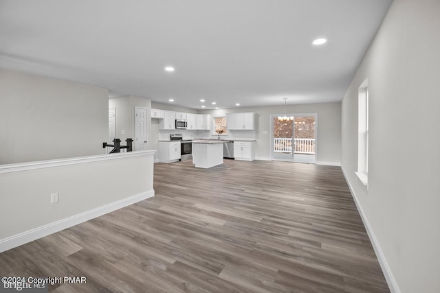 unfurnished living room featuring recessed lighting, wood finished floors, baseboards, and an inviting chandelier