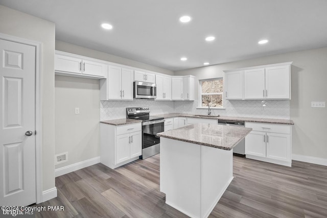 kitchen featuring appliances with stainless steel finishes, light stone countertops, white cabinetry, and wood finished floors