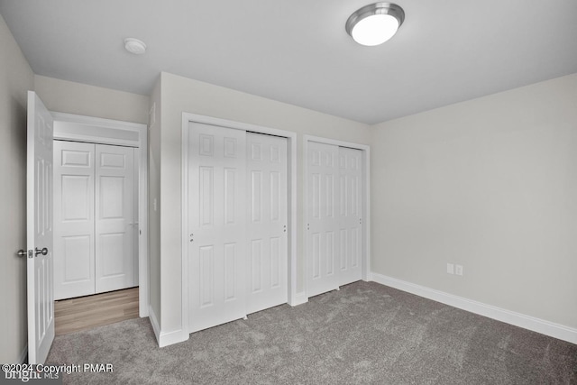 unfurnished bedroom featuring carpet floors, two closets, and baseboards