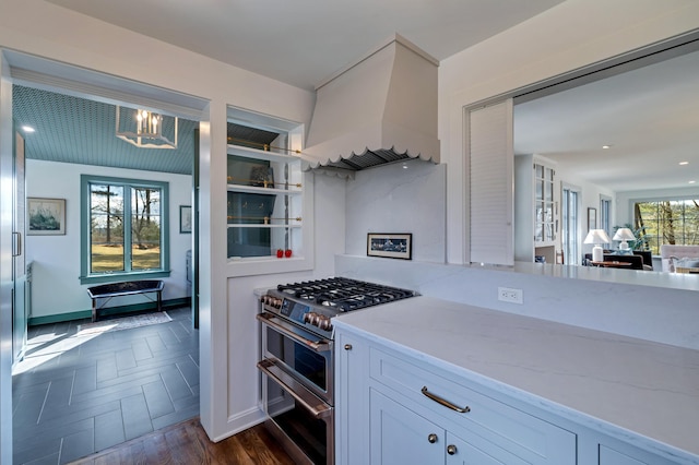 kitchen with custom range hood, light stone counters, double oven range, white cabinets, and baseboards