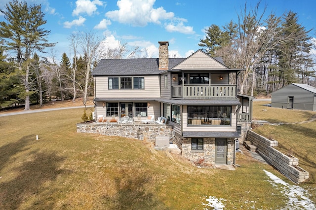 rear view of property featuring a yard, stone siding, a balcony, and a chimney