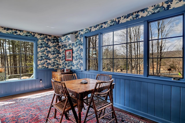 dining room with a wainscoted wall, an AC wall unit, wallpapered walls, and wood finished floors