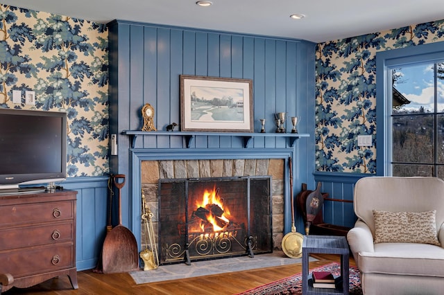 living room featuring a wainscoted wall, a lit fireplace, wood finished floors, and wallpapered walls