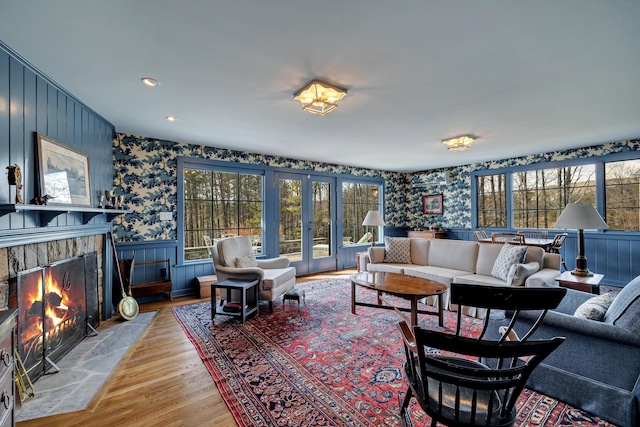 living area with a tiled fireplace, a healthy amount of sunlight, wallpapered walls, and wood finished floors