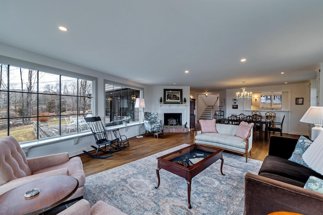 living room with recessed lighting, a notable chandelier, a fireplace with raised hearth, and wood finished floors