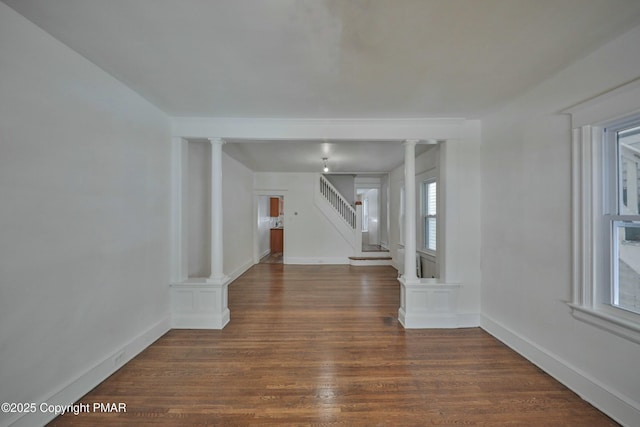 spare room with baseboards, stairway, ornate columns, and wood finished floors