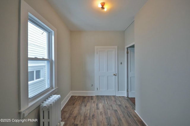 spare room featuring dark wood-type flooring, baseboards, and radiator heating unit