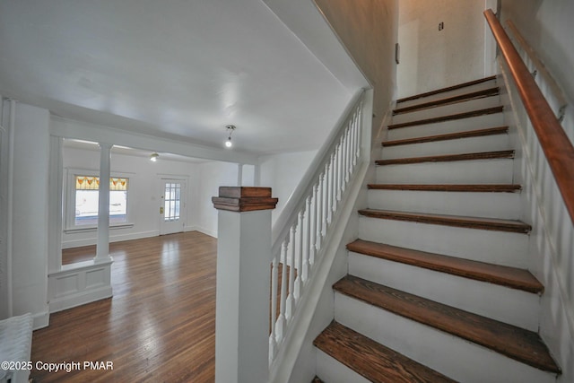 staircase featuring decorative columns, baseboards, and wood finished floors