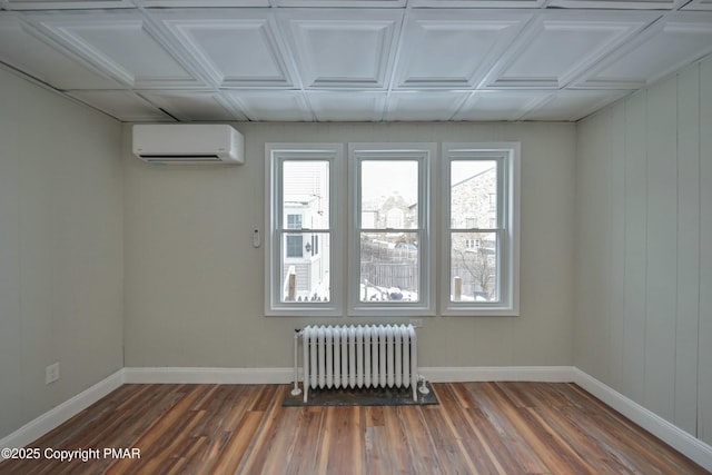 empty room with radiator heating unit, a wall mounted air conditioner, wood finished floors, and baseboards