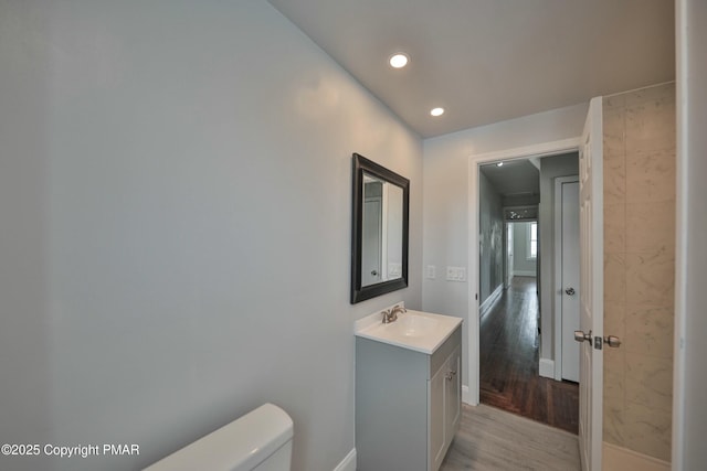 half bathroom with baseboards, toilet, wood finished floors, vanity, and recessed lighting