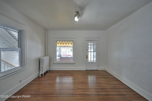 empty room with dark wood-type flooring and radiator heating unit