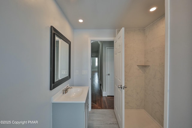 full bathroom with tiled shower, wood finished floors, vanity, and recessed lighting