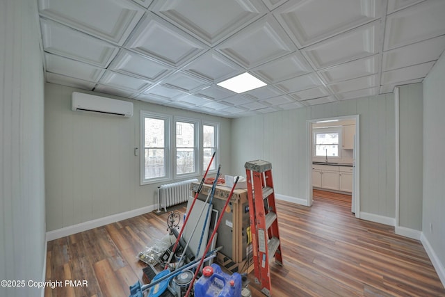 game room featuring a wall unit AC, radiator, baseboards, and wood finished floors