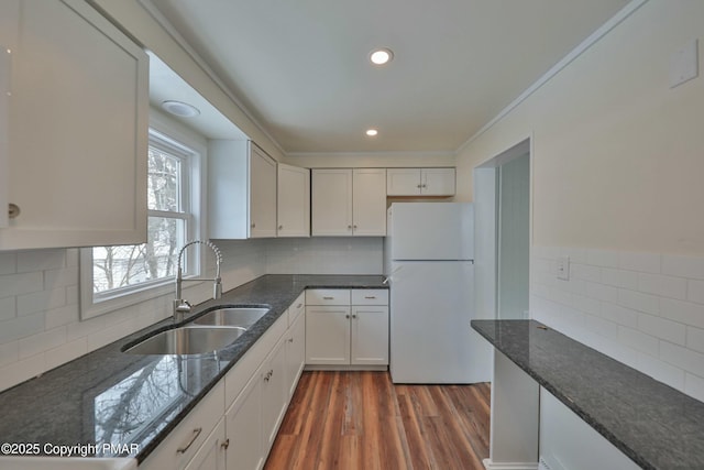 kitchen featuring wood finished floors, a sink, white cabinetry, freestanding refrigerator, and dark stone countertops