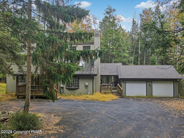 view of front of house featuring a garage, roof with shingles, a deck, and driveway