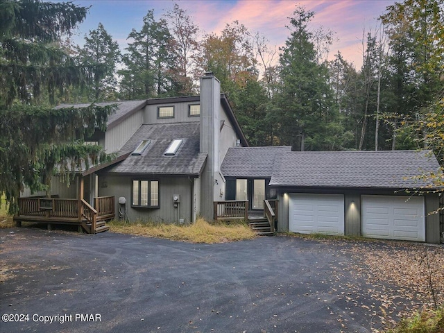 view of front of home featuring a deck, driveway, roof with shingles, a garage, and a chimney