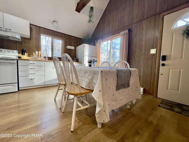 kitchen with lofted ceiling, wooden walls, under cabinet range hood, white appliances, and light wood finished floors