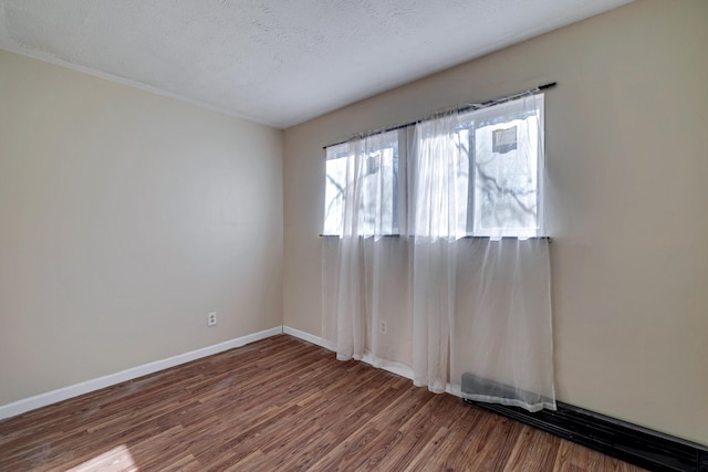 spare room featuring a textured ceiling, baseboards, and wood finished floors