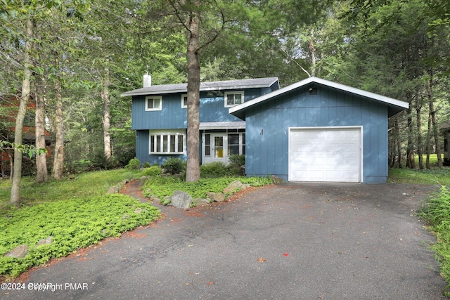 view of front of property featuring aphalt driveway, a wooded view, and a garage