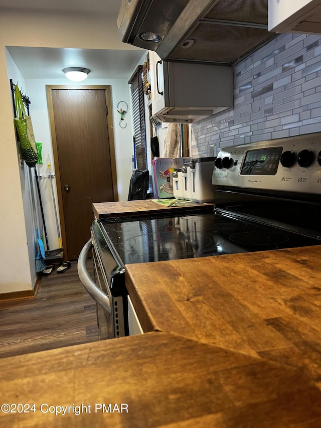 kitchen featuring dark wood-type flooring, butcher block counters, under cabinet range hood, and decorative backsplash