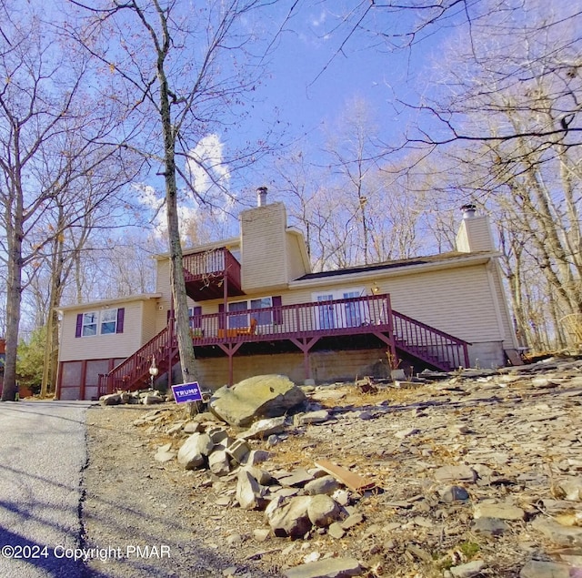 view of front of property featuring aphalt driveway, a chimney, an attached garage, a deck, and stairs