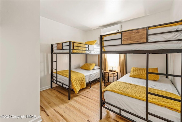 bedroom featuring wood finished floors, baseboards, and a wall mounted AC