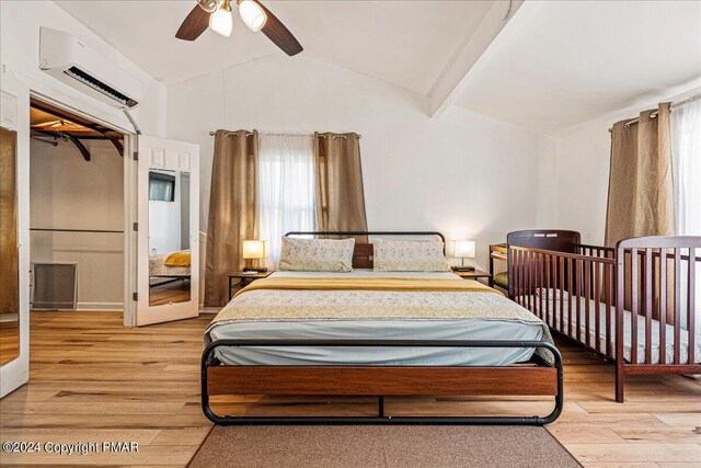 bedroom featuring light wood-style floors, a wall mounted air conditioner, lofted ceiling with beams, and a ceiling fan