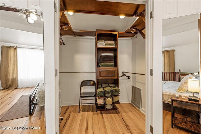 walk in closet featuring light wood finished floors, beam ceiling, and visible vents