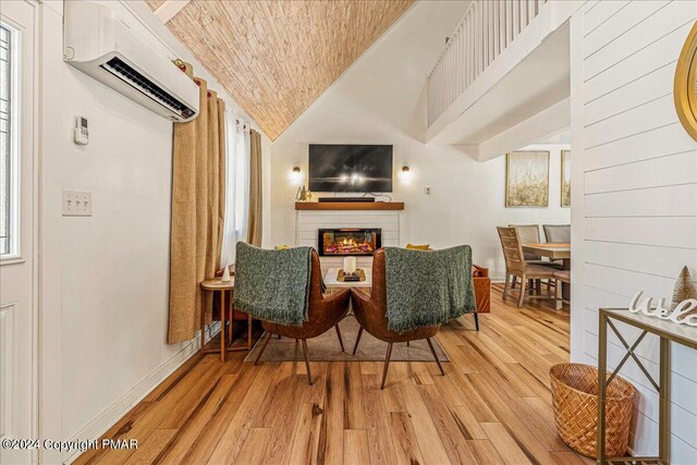 sitting room featuring baseboards, vaulted ceiling, an AC wall unit, light wood-type flooring, and a glass covered fireplace