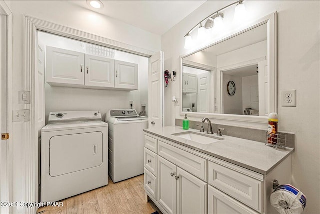 laundry room featuring cabinet space, light wood finished floors, a sink, and washing machine and clothes dryer