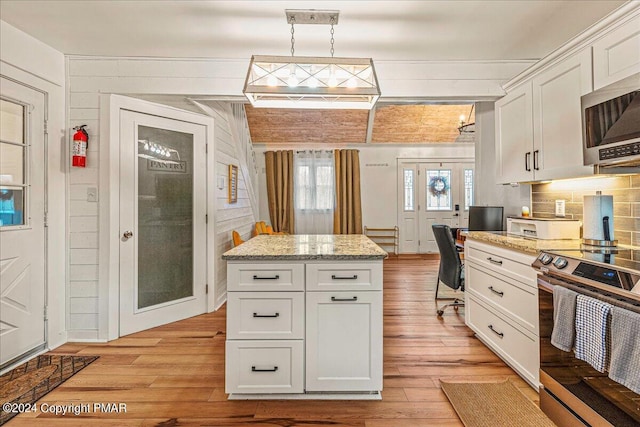 kitchen featuring decorative light fixtures, stainless steel appliances, light wood-type flooring, white cabinetry, and backsplash