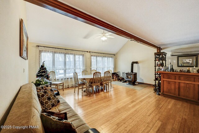 living room with lofted ceiling with beams, ceiling fan, light hardwood / wood-style floors, and a wood stove