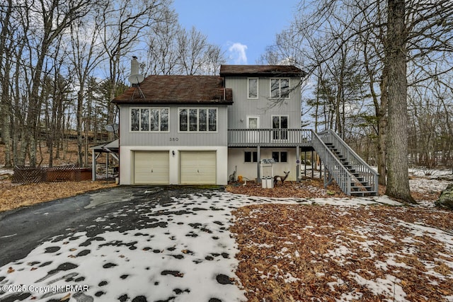 back of property with driveway, an attached garage, a chimney, and stairway