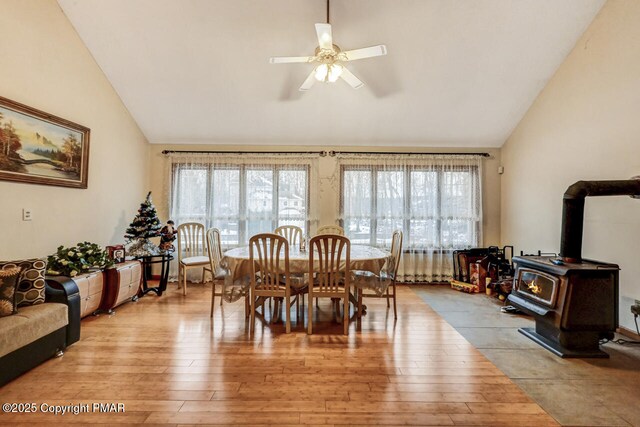 dining room with light hardwood / wood-style floors, vaulted ceiling, a wood stove, and a wealth of natural light